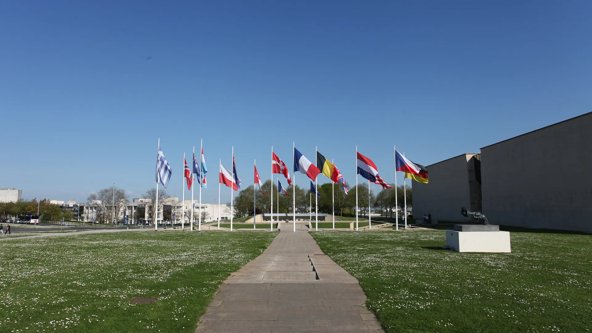 Path across the lawn of the Mémorial de Caen esplanade towards a line of national flags