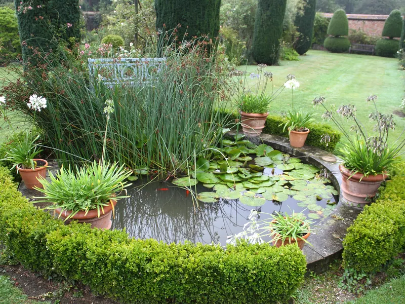 Lily pond surrounded by potted plants and hedges at Bois des Moutiers, Varengeville