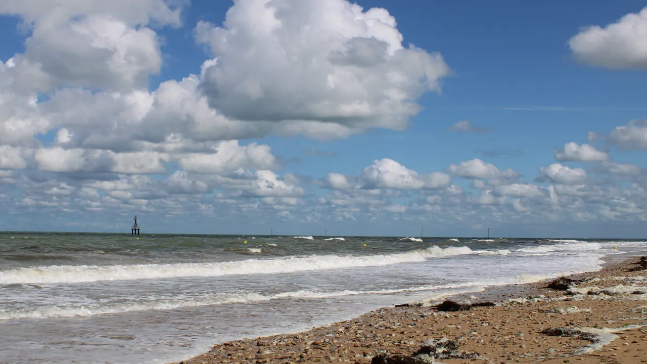 Juno Beach shoreline at Courseulles-sur-Mer with waves and scattered clouds