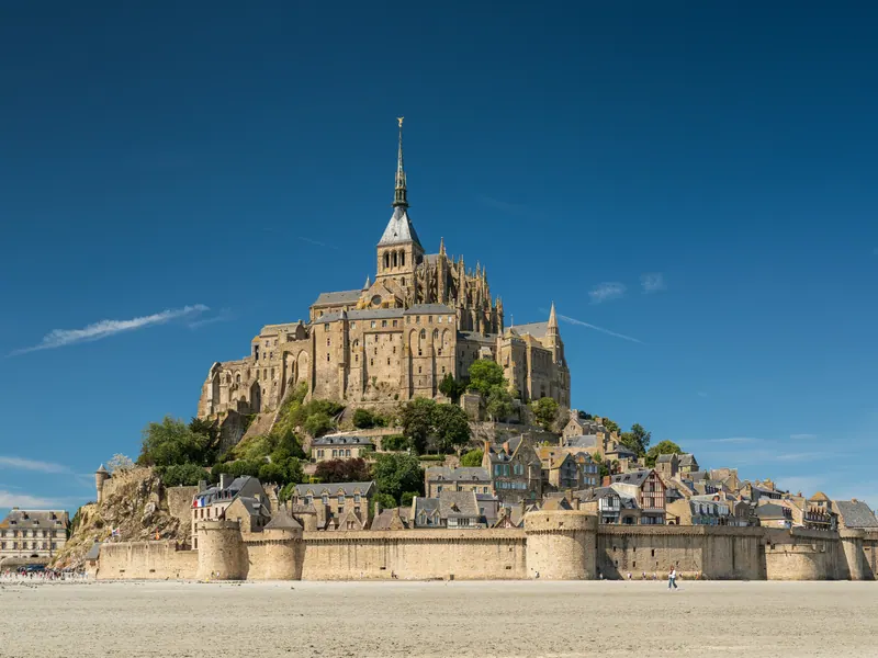 Mont-Saint-Michel abbey and village seen from the sands of the bay under blue sky
