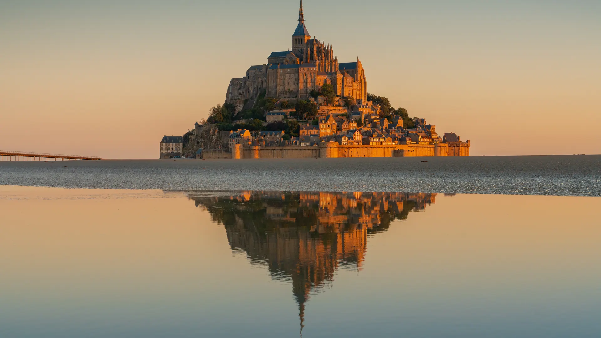 Mont-Saint-Michel and its abbey at sunrise, reflected in shallow water on the bay