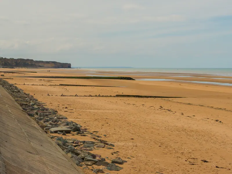 Wide sandy Omaha Beach at low tide with a sea wall and distant bluffs