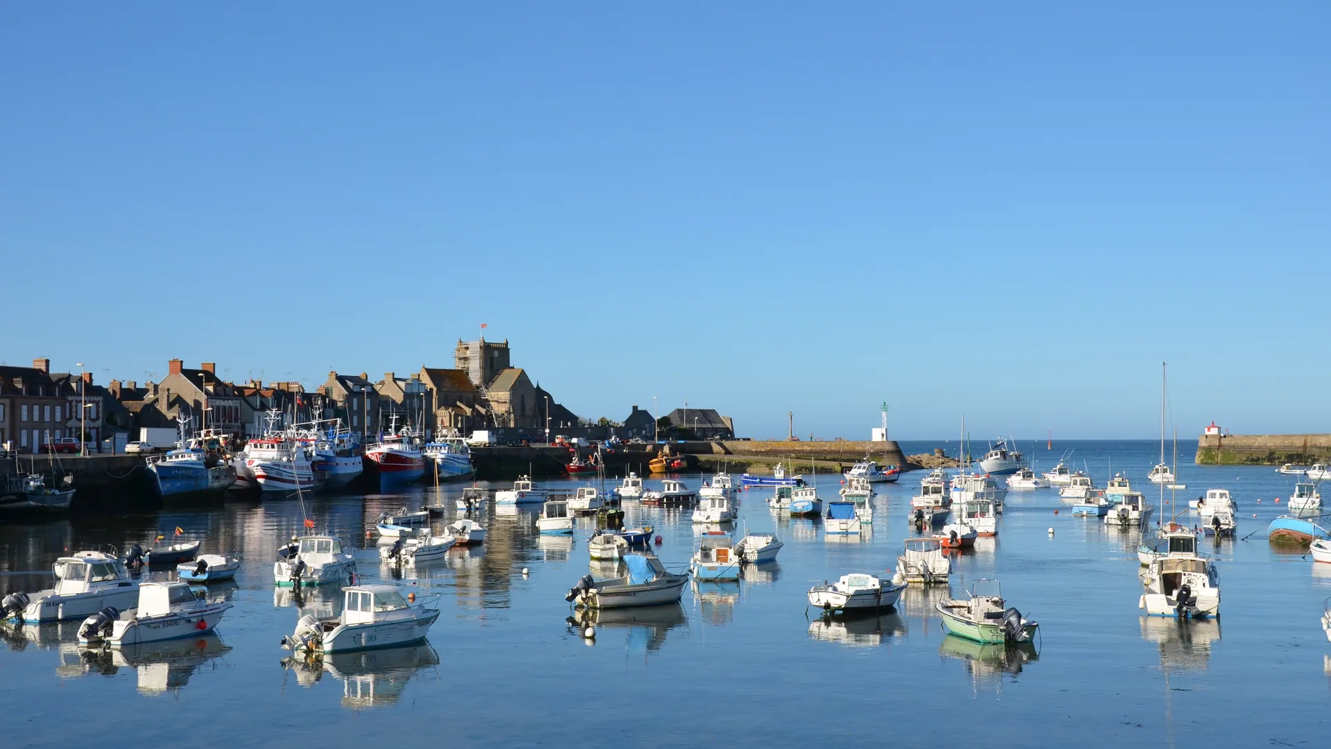 Small boats moored in Barfleur harbour with the stone village behind